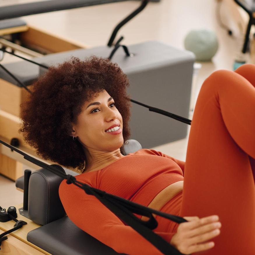 A woman practices pilates on a reformer, enhancing her fitness and flexibility in a vibrant studio.